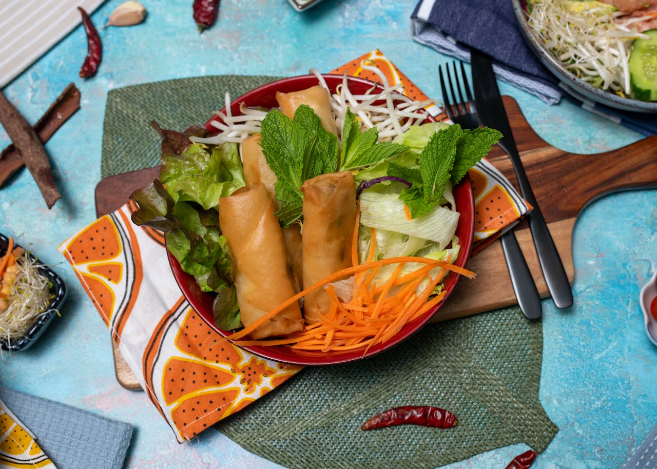 Colorful vegan spring rolls and fresh salad on a vibrant table setting.
