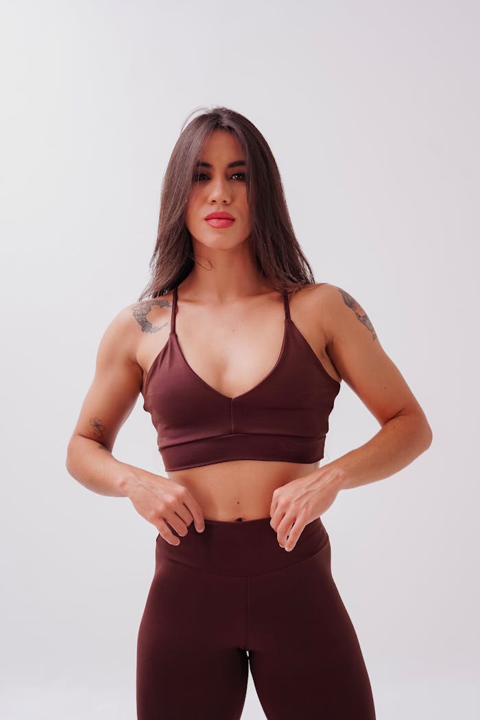 Confident woman in brown activewear posing against a neutral backdrop, showcasing fitness and fashion.